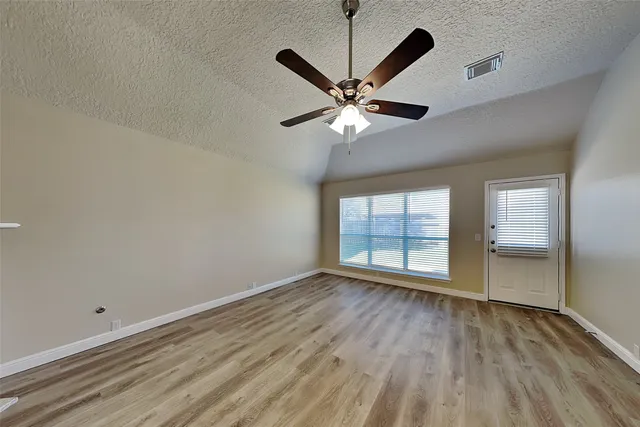 an empty room with wooden floor fan and windows