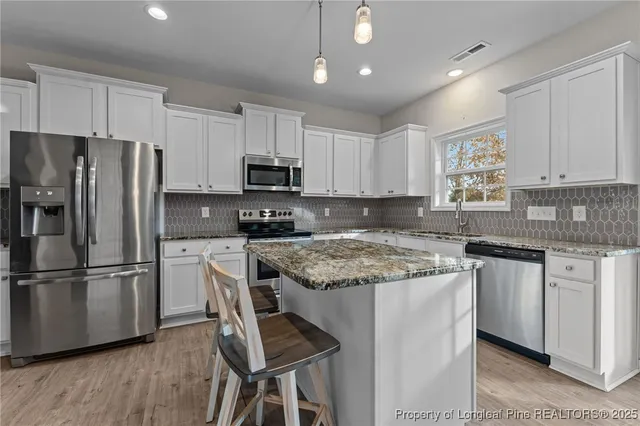 a kitchen with stainless steel appliances granite countertop a stove top oven a refrigerator a sink and dishwasher with wooden floor