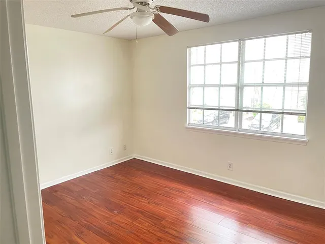 an empty room with wooden floor chandelier fan and windows