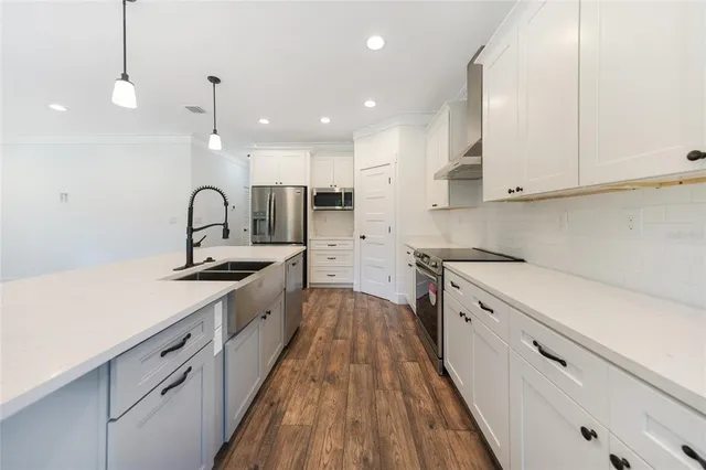 a large kitchen with stainless steel appliances a large counter top a stove a sink dishwasher and a refrigerator with wooden floor