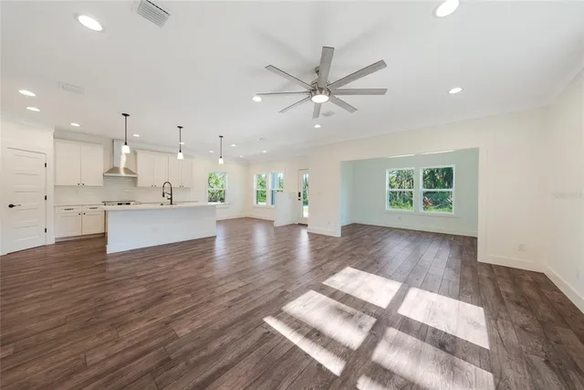 a view of an empty room and kitchen with wooden floor and a window
