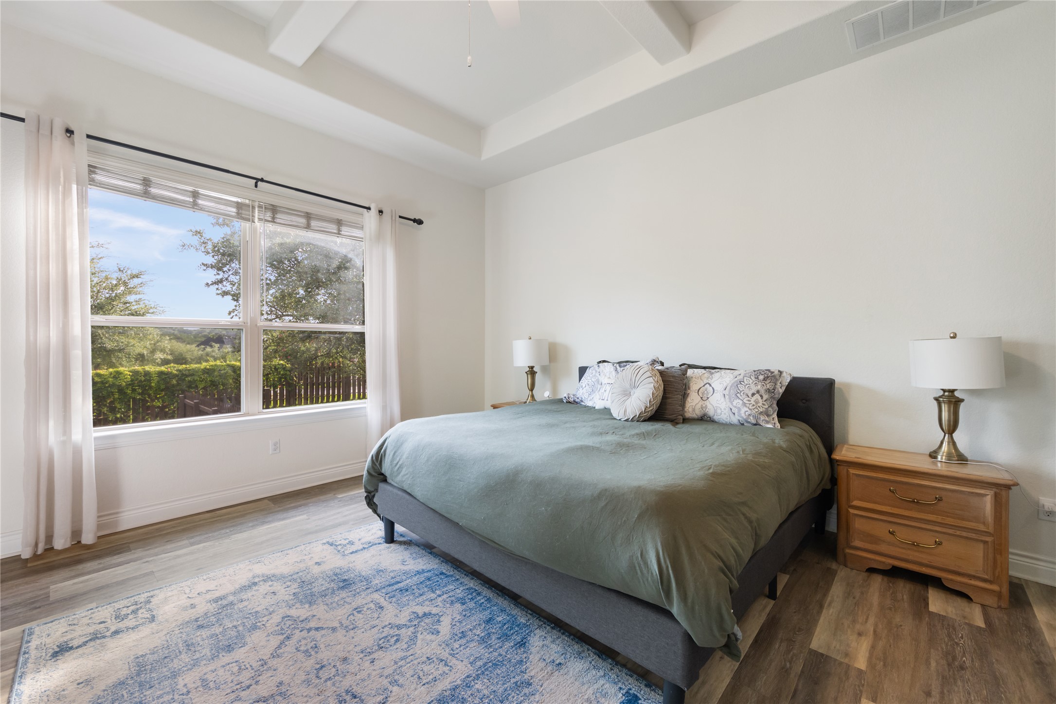 415 Bitterroot Lane Austin, TX 78737 - Photo 11 of 25 A spacious bedroom retreat features large windows overlooking lush greenery and elegant tray ceilings.