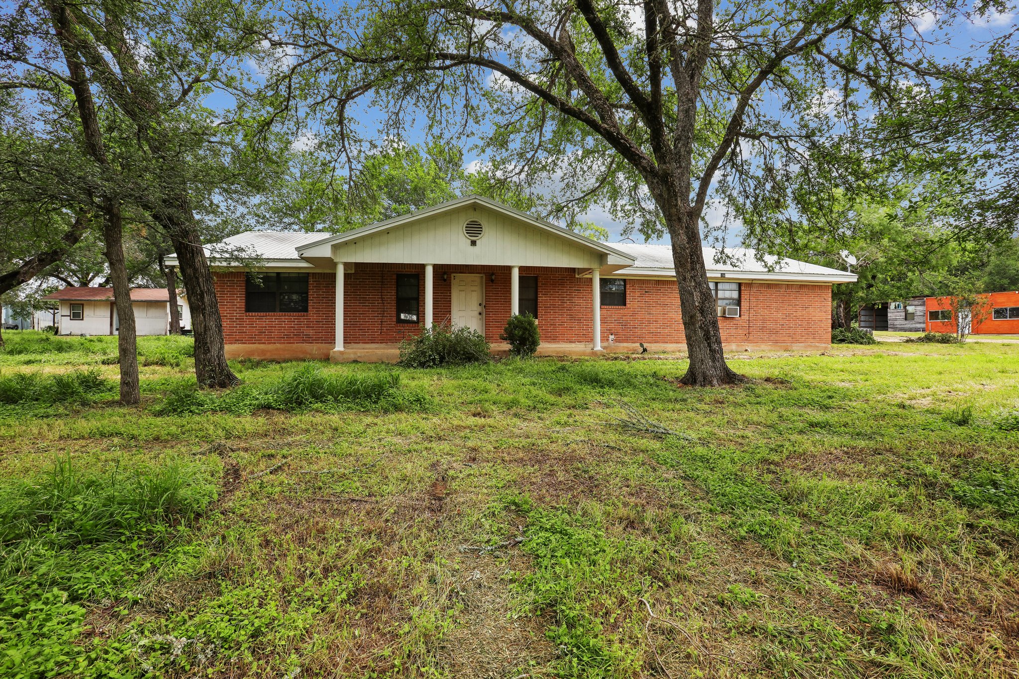406 Monkey Road Elgin, TX 78621 - Photo 3 of 39 Brick exterior home featuring a covered front porch with white columns, a gable roof accent, and mature trees in the front yard
