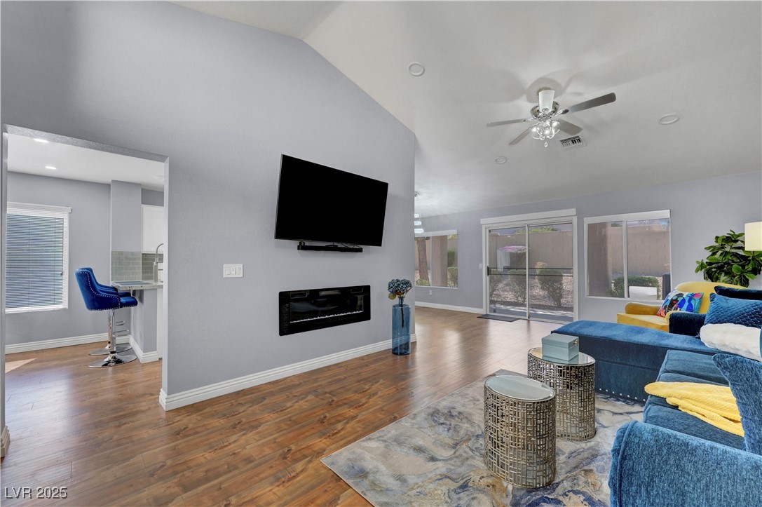 Living area with wood finished floors, lofted ceiling, a ceiling fan, a glass covered fireplace, and recessed lighting