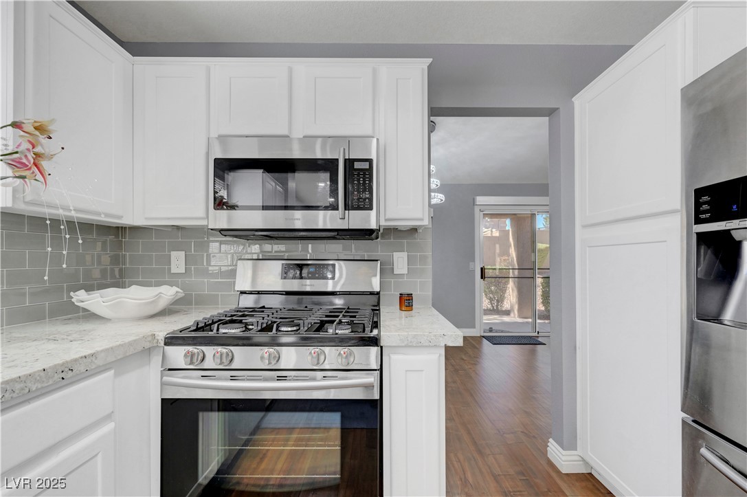 Undisclosed Address Las Vegas, NV 89134 - Photo 25 of 39 Kitchen featuring stainless steel appliances, white cabinetry, decorative backsplash, dark wood-style flooring, and light stone countertops