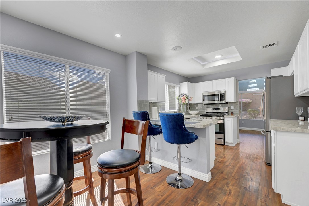 Undisclosed Address Las Vegas, NV 89134 - Photo 8 of 39 Kitchen with a breakfast bar area, appliances with stainless steel finishes, white cabinets, dark wood-style flooring, and a raised ceiling