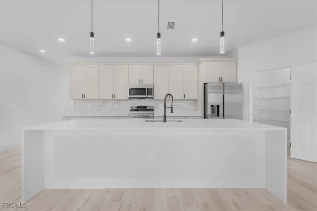 a large kitchen with stainless steel appliances a refrigerator a stove a sink and white cabinets