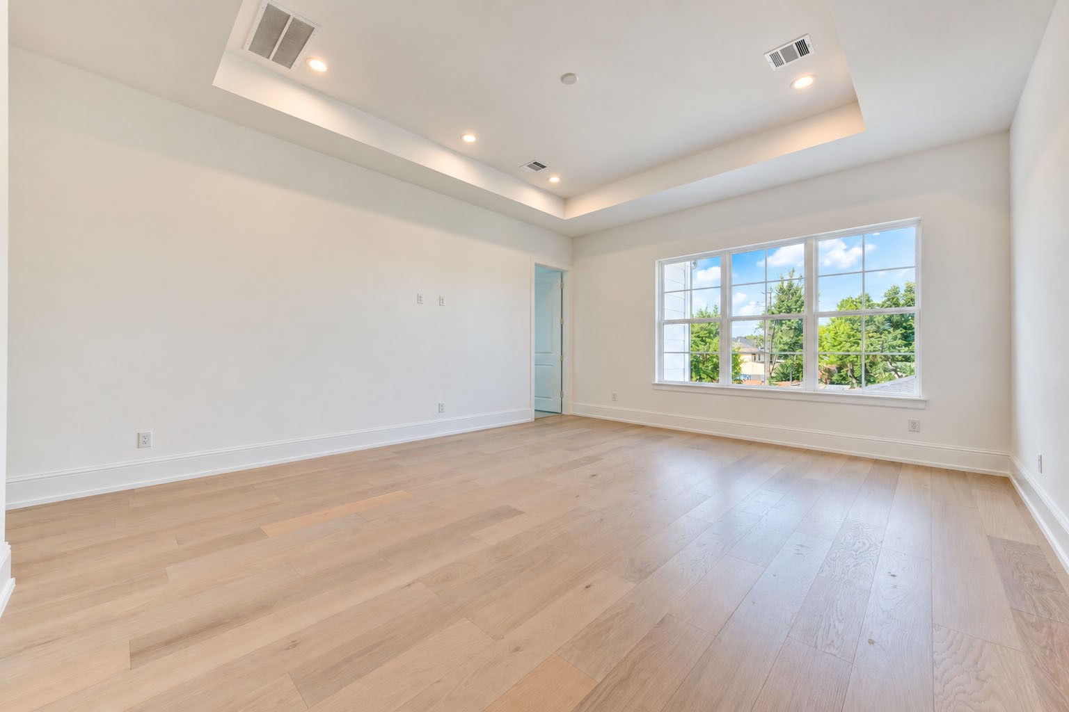 2309 Hollister Road Houston, TX 77080 - Photo 20 of 47 Another view of the spacious upstairs game room showcases a dramatic tray ceiling, warm wide-plank flooring, and an expansive wall of windows framing treetop views and filling the room with natural light. Generous proportions offer exceptional flexibility for a media lounge, billiards, game tables, or a stylish second living area designed for relaxation and entertaining.