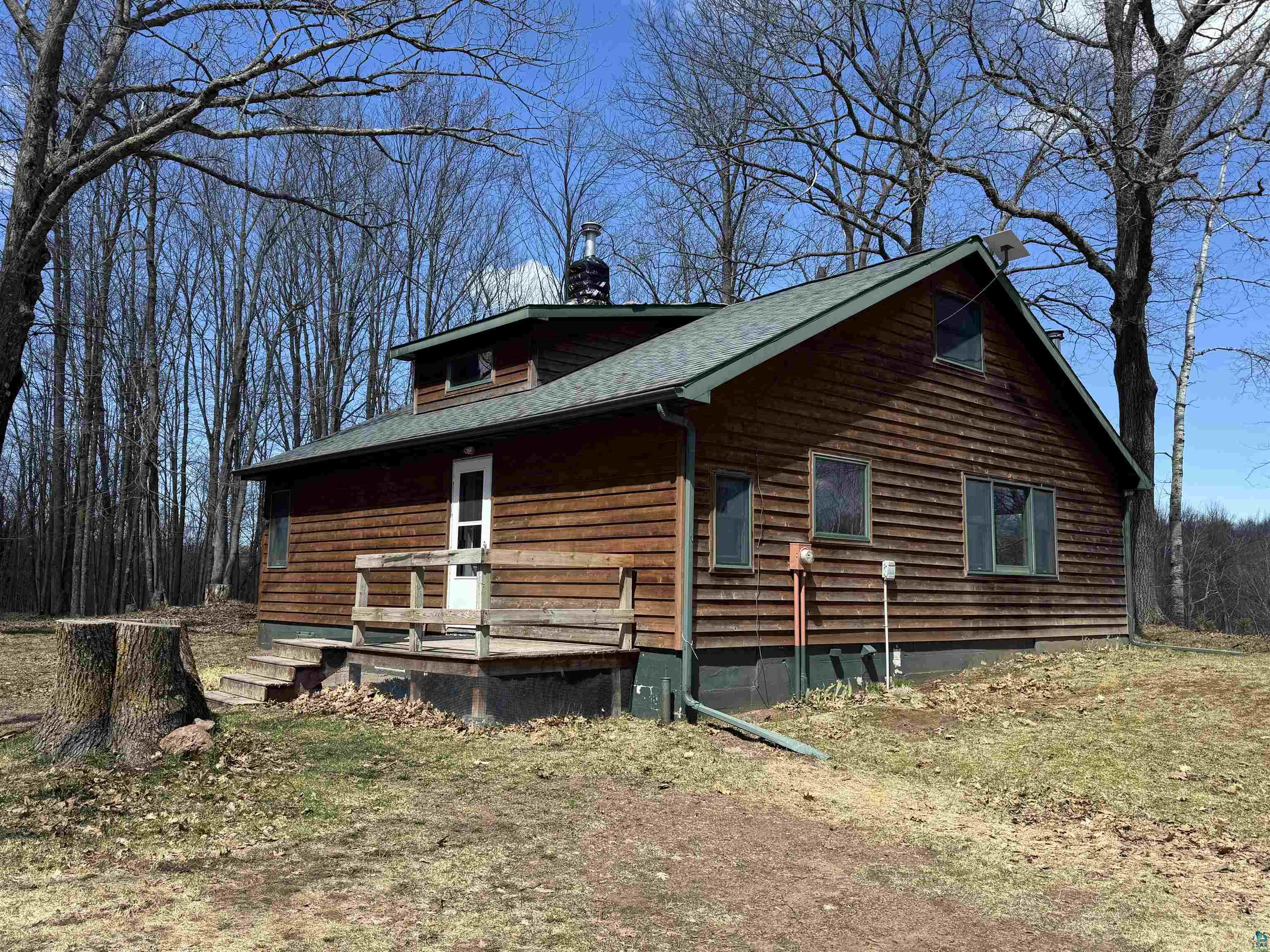 Wood-sided residence featuring a green asphalt shingle roof, a front porch with natural wood railings, and multiple windows