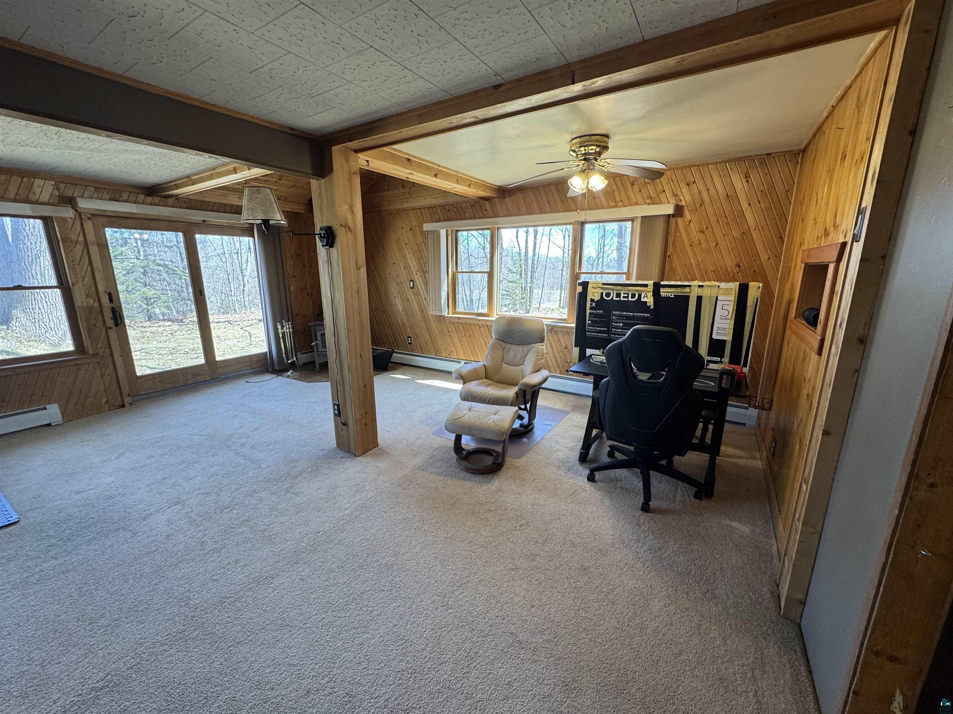 4897 Swanson Drive Maple, WI 54854 - Photo 12 of 25 Spacious room featuring wood plank wall paneling, light-colored carpeting, exposed structural beams, and multiple windows.
