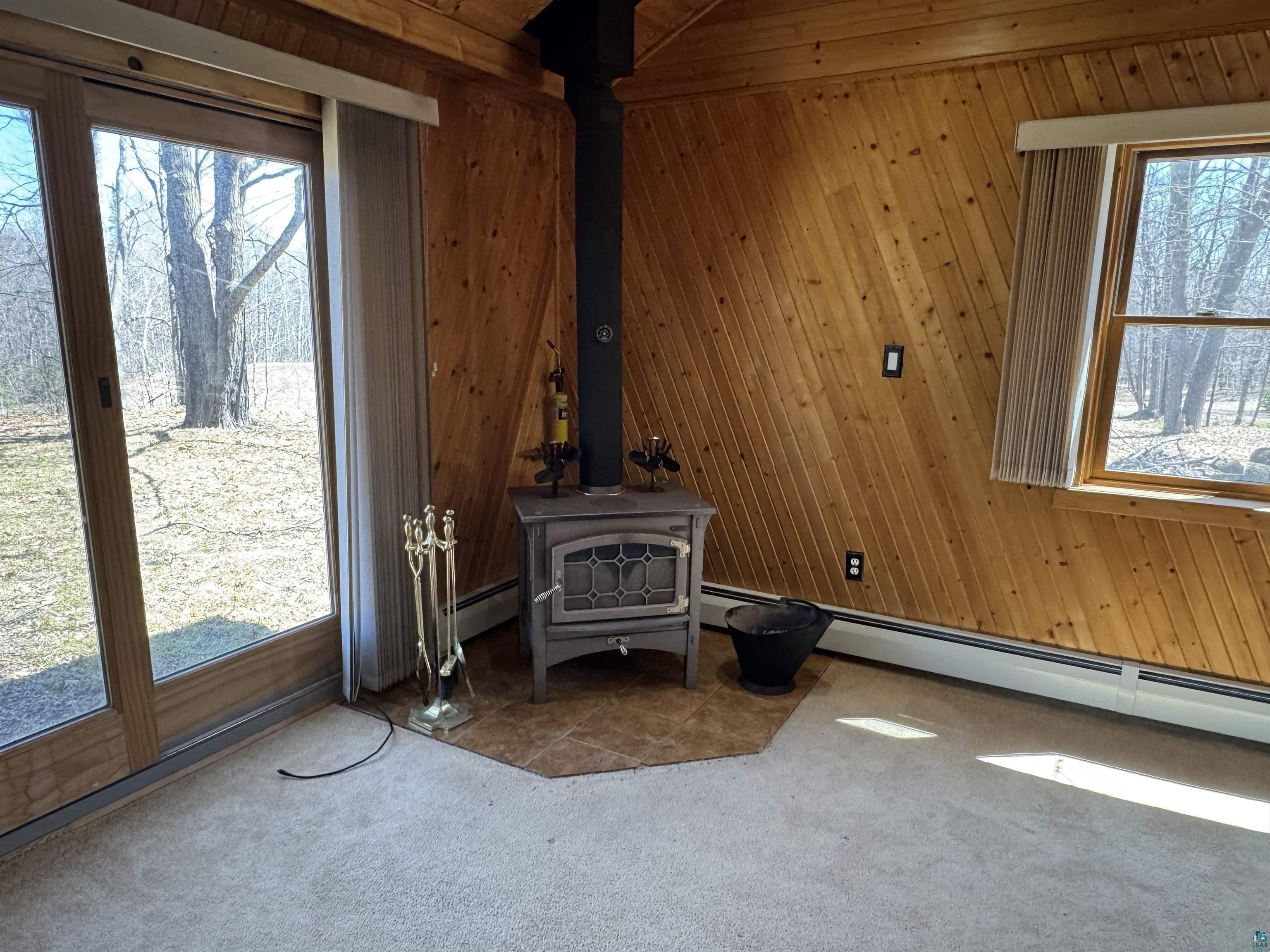 4897 Swanson Drive Maple, WI 54854 - Photo 15 of 25 Interior room featuring a wood-burning stove with a black stovepipe, wood-paneled walls, and carpet flooring
