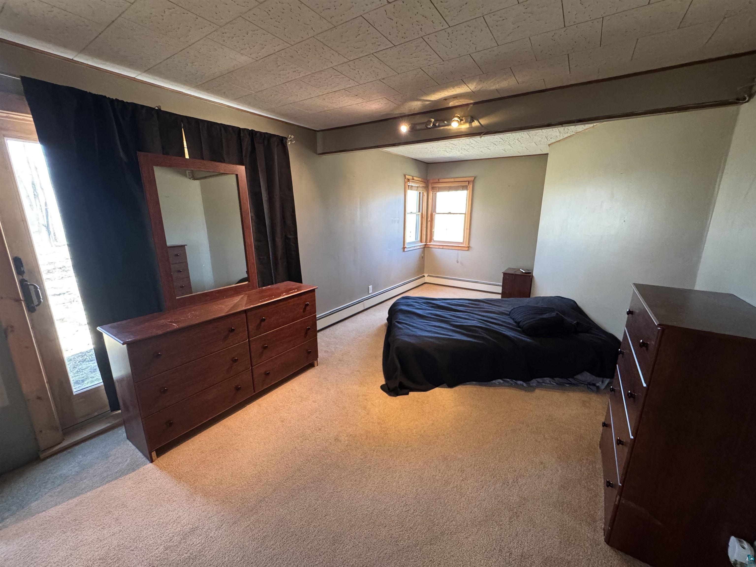 4897 Swanson Drive Maple, WI 54854 - Photo 8 of 25 Spacious primary bedroom on main floor with plush carpeting, natural wood-frame windows, patio door, baseboard heating