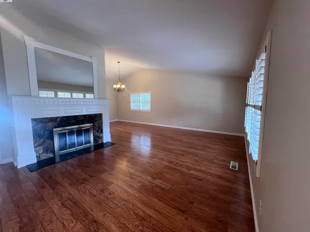 a view of an empty room with wooden floor fireplace and a window