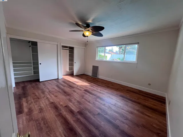 a view of empty room with wooden floor and fan