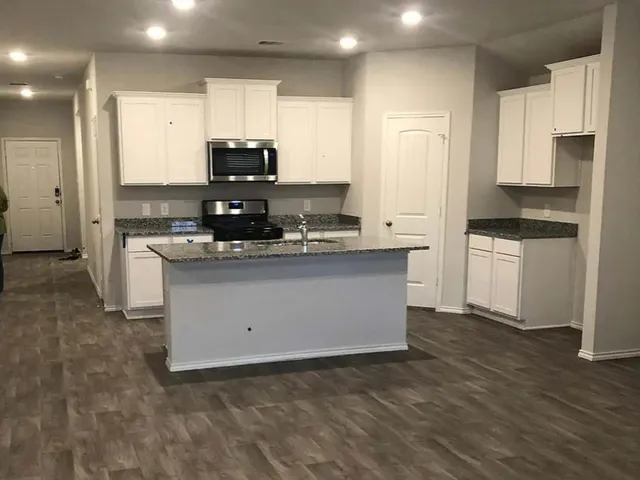 a kitchen with kitchen island granite countertop a stove top oven a sink and white cabinets