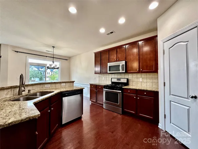 a kitchen with stainless steel appliances granite countertop wooden cabinets a sink dishwasher a stove and a refrigerator with wooden floor