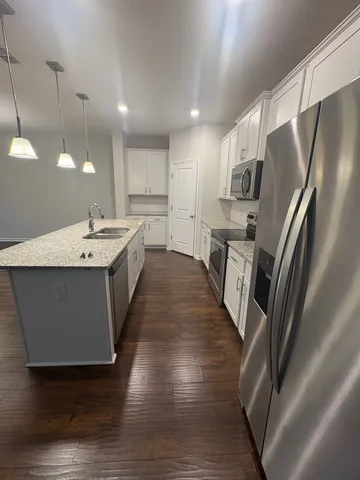 a large kitchen with stainless steel appliances a refrigerator a sink dishwasher a oven with white cabinets and wooden floor