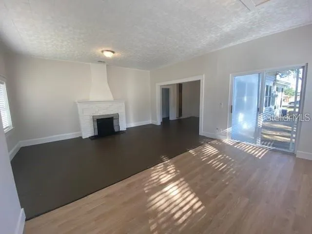 a view of an empty room with wooden floor fireplace and a window