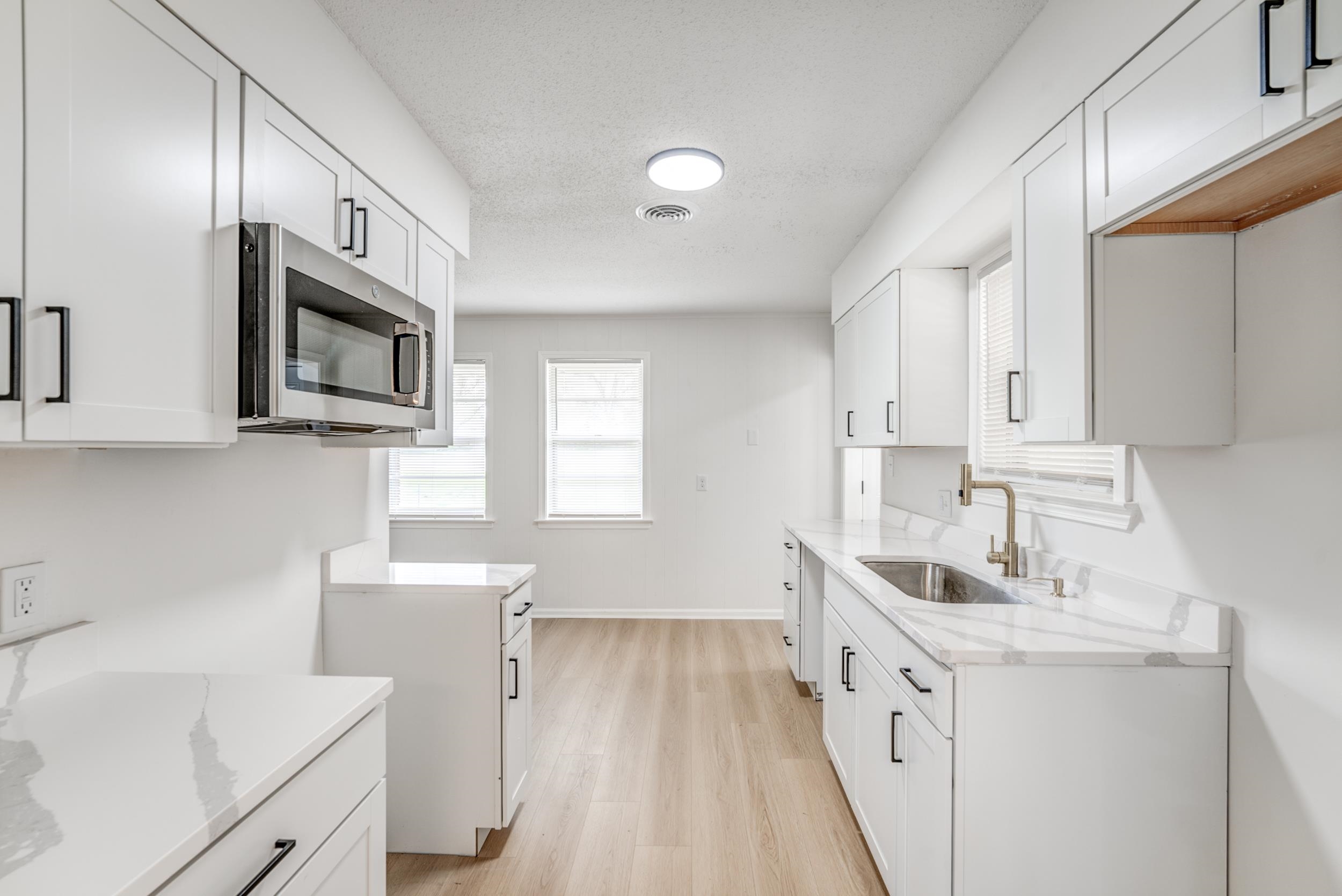 5156 Windcrest Road Memphis, TN 38116 - Photo 7 of 24 Kitchen featuring white cabinets, stainless steel microwave, light stone counters, light wood-style floors, and a textured ceiling
