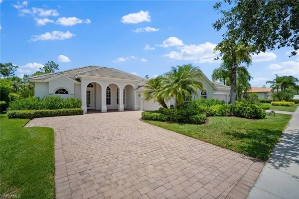 a white house with a big yard plants and large trees
