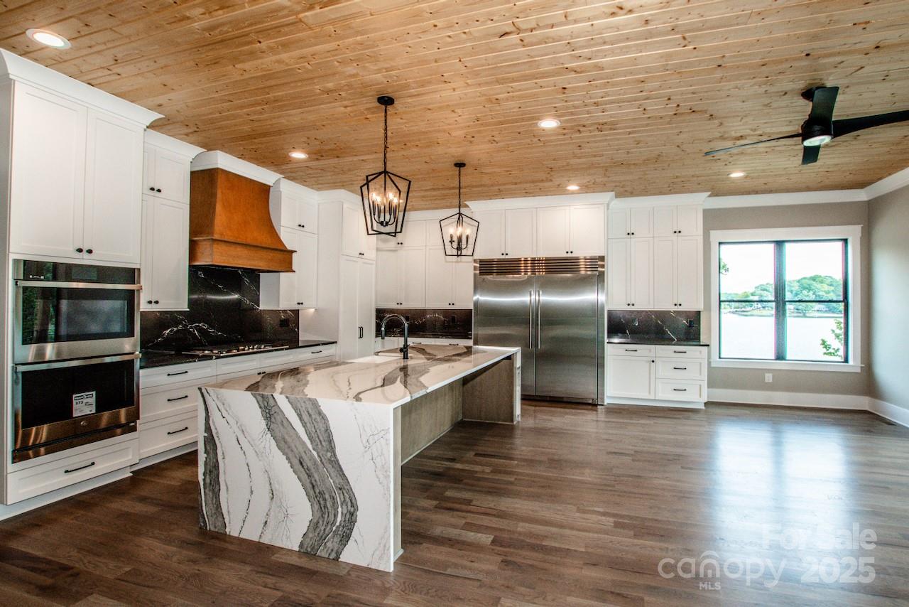 110 Emmaline Court Troutman, NC 28166 - Photo 12 of 40 a large kitchen with stainless steel appliances kitchen island granite countertop a stove a sink a refrigerator and white cabinets with wooden floor