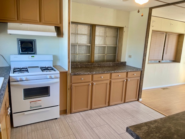 5075 Mountain View Road Fort Mohave, AZ 86426 - Photo 10 of 27 Kitchen featuring a white gas range with overhead hood, wood-finish cabinetry, and a countertop with integrated sink