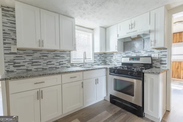 a kitchen with stainless steel appliances granite countertop a stove a sink and white cabinets