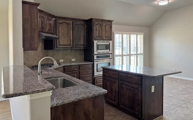 a kitchen with granite countertop a sink wooden cabinets and stainless steel appliances