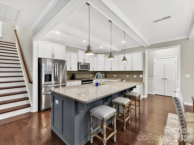 a kitchen with stainless steel appliances kitchen island granite countertop a table chairs in it and wooden floors