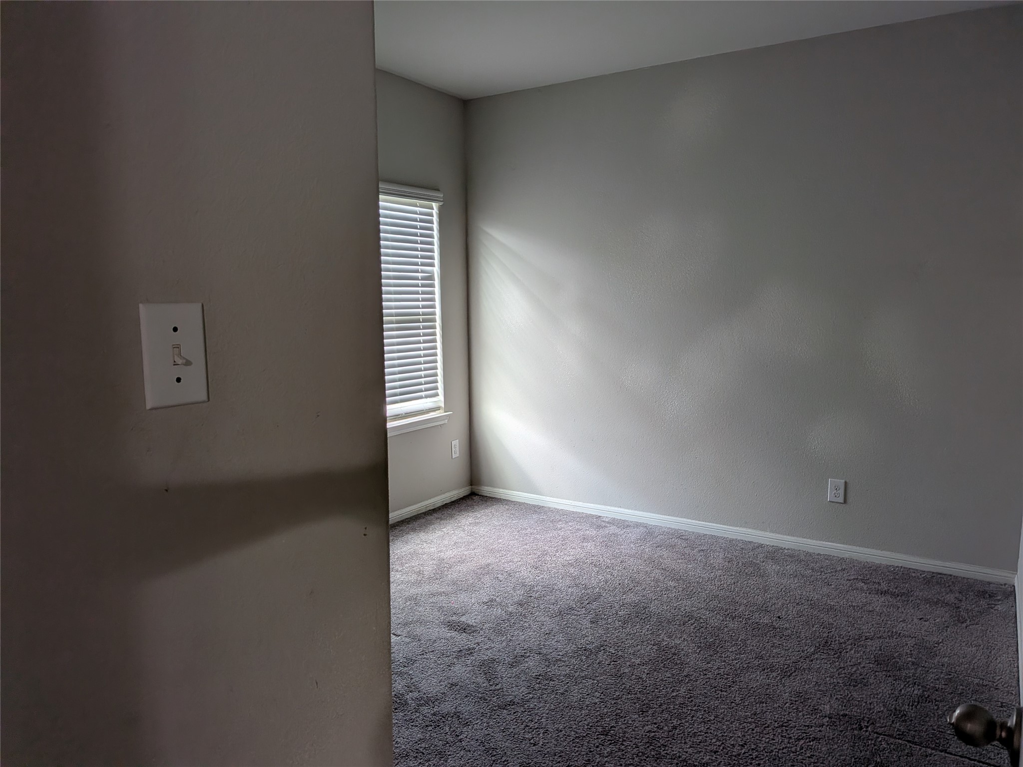 15730 Joe Dimaggio Street Splendora, TX 77372 - Photo 14 of 20 This photo shows a small, carpeted room with neutral-colored walls, a window with blinds allowing natural light, and a light switch on the wall.