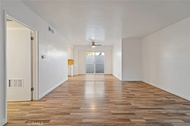 a view of an empty room with wooden floor and kitchen view