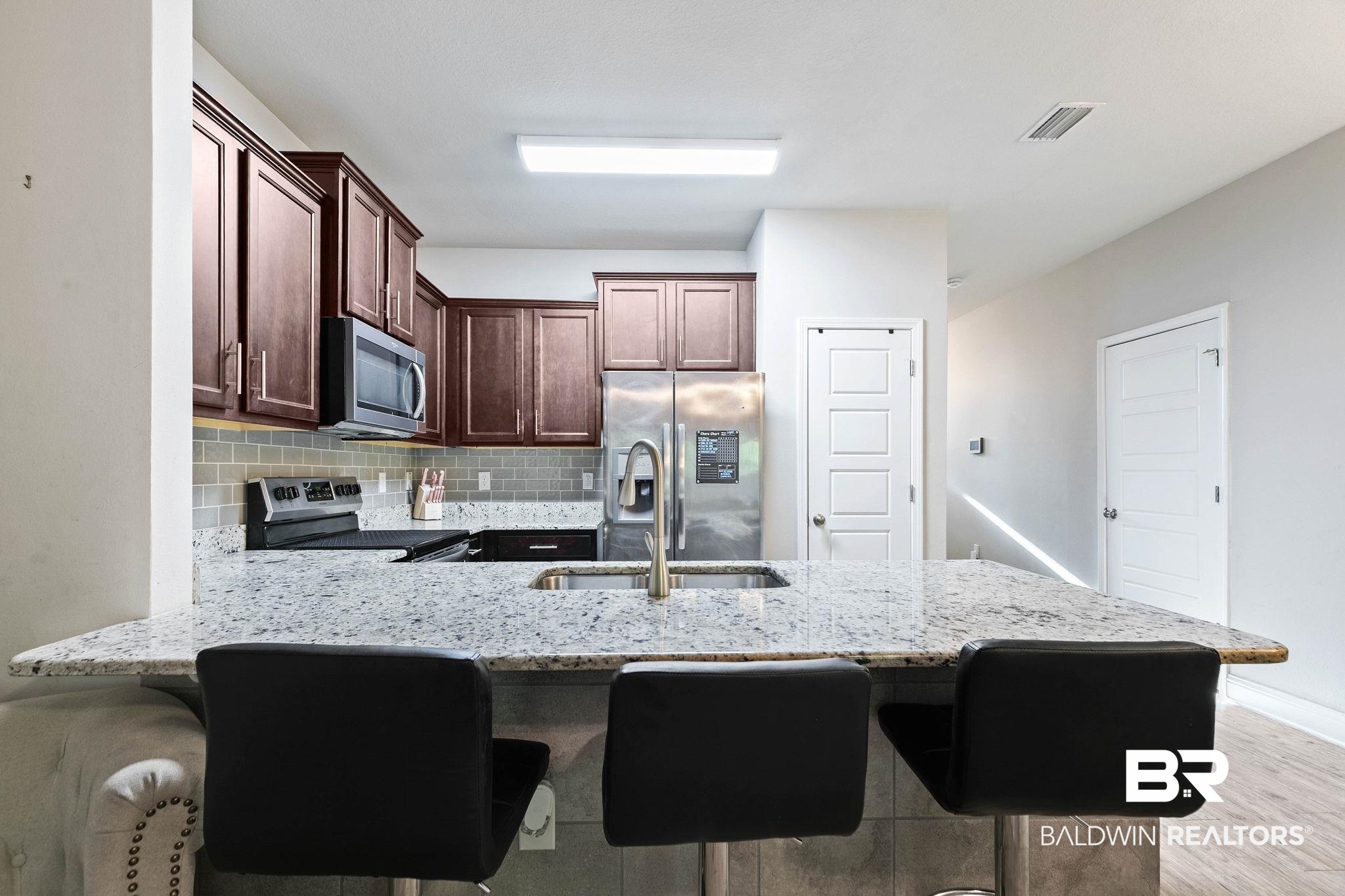 25806 Pollard Road, Unit 24 Daphne, AL 36526 - Photo 8 of 33 Kitchen with backsplash, a kitchen breakfast bar, light stone countertops, a peninsula, and appliances with stainless steel finishes