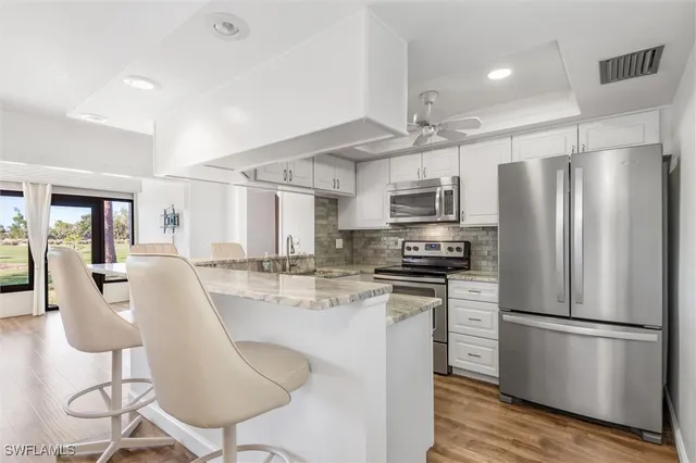 a kitchen with stainless steel appliances granite countertop a refrigerator a stove top oven a sink dishwasher a dining table and chairs with wooden floor