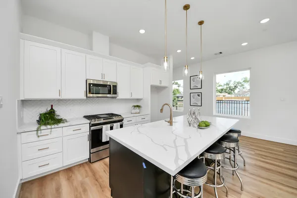 a kitchen with stainless steel appliances kitchen island granite countertop white cabinets a stove a sink a dining table and chairs