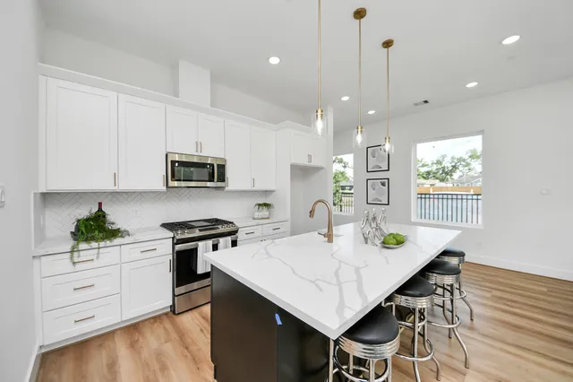 a kitchen with stainless steel appliances kitchen island granite countertop white cabinets a stove a sink a dining table and chairs