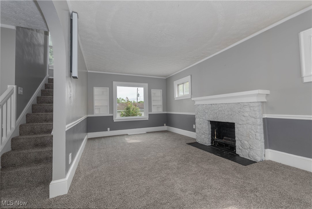 197 East Wilbeth Road Akron, OH 44301 - Photo 9 of 22 Unfurnished living room with carpet, stairs, a stone fireplace, a textured ceiling, and crown molding