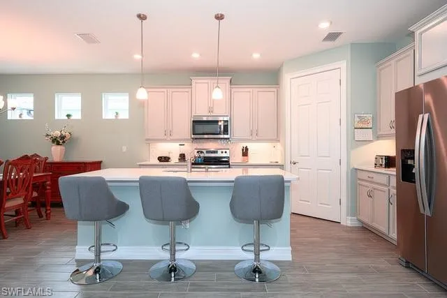 a kitchen with stainless steel appliances granite countertop a refrigerator a stove top oven a sink dishwasher a dining table and chairs with wooden floor