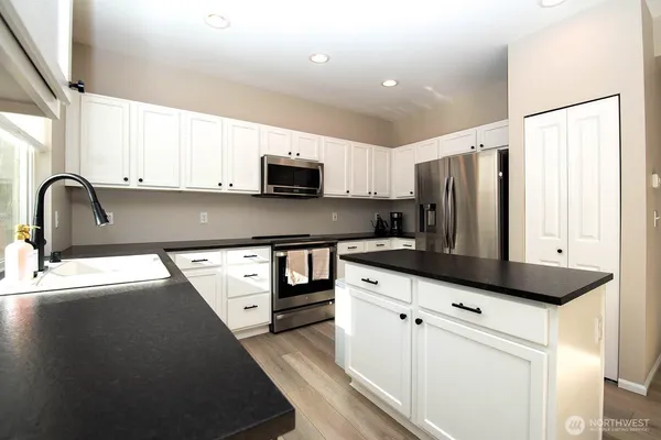 a kitchen with stainless steel appliances a sink a stove a microwave a refrigerator a counter space and cabinets