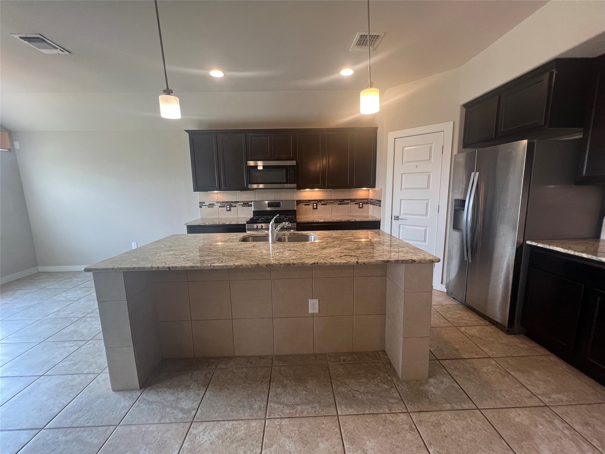 7009 Sienna Rouge Path Austin, TX 78744 - Photo 3 of 29 Kitchen featuring light stone countertops, stainless steel appliances, decorative light fixtures, a kitchen island with sink, and light tile patterned floors