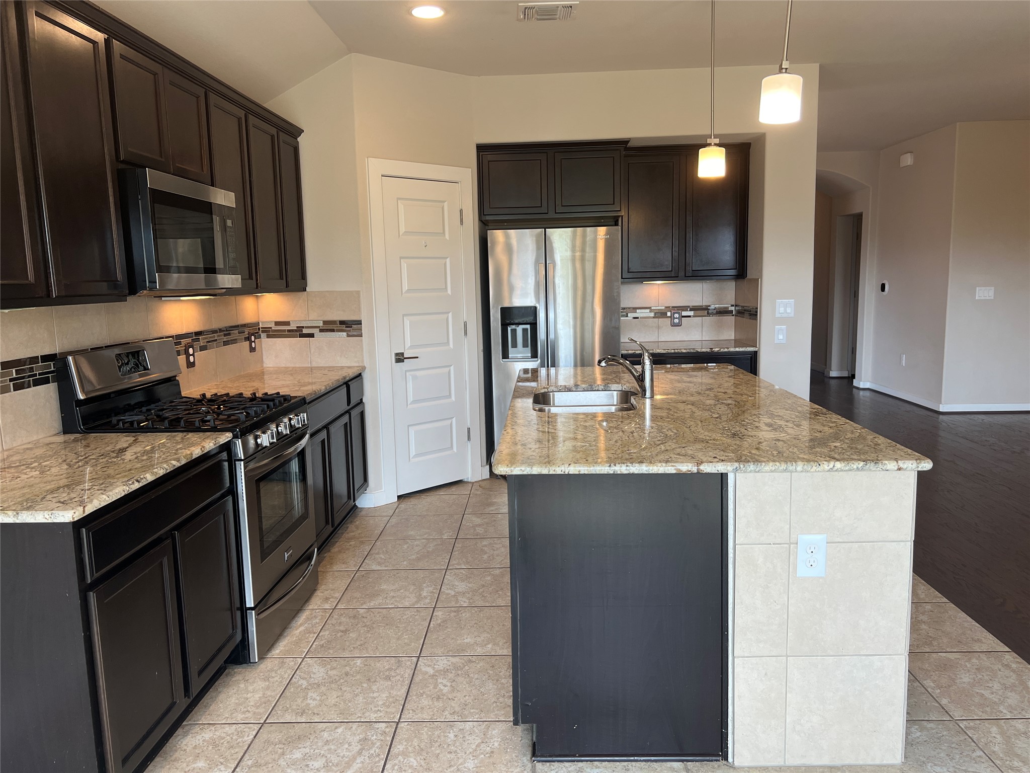 7009 Sienna Rouge Path Austin, TX 78744 - Photo 5 of 29 Kitchen featuring stainless steel appliances, arched walkways, decorative backsplash, a center island with sink, and dark wood finish cabinetry