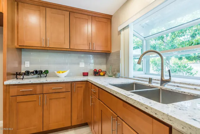 a kitchen with granite countertop a sink stainless steel appliances white cabinets and a window