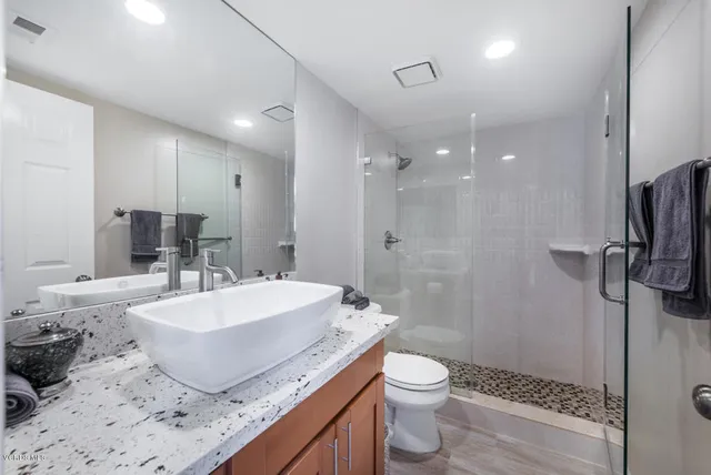 a bathroom with a granite countertop sink a toilet a mirror and shower