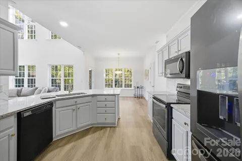 a kitchen with stainless steel appliances granite countertop a stove top oven a sink dishwasher a dining table and chairs with wooden floor