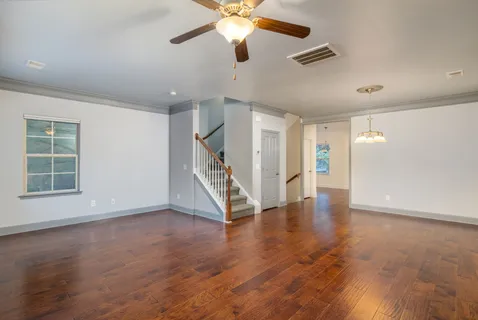 a view of an empty room with wooden floor ceiling fan and a window