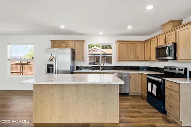 a kitchen with stainless steel appliances granite countertop a refrigerator a stove and a sink with wooden floor