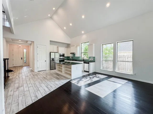 a large open kitchen with kitchen island a refrigerator a stove a sink dishwasher and wooden cabinets with wooden floor