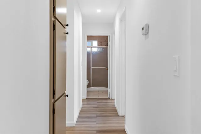 a view of a hallway with wooden floor and a bathroom