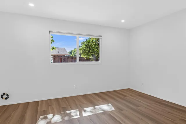 a view of an empty room with wooden floor and a window