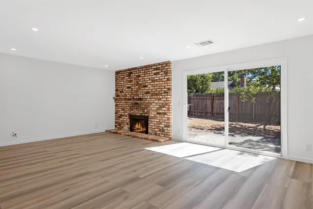 a view of an empty room with wooden floor and a fireplace