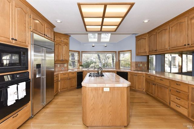 a large kitchen with stainless steel appliances kitchen island granite countertop a refrigerator a stove top oven a sink with a dining table and chairs with wooden floor